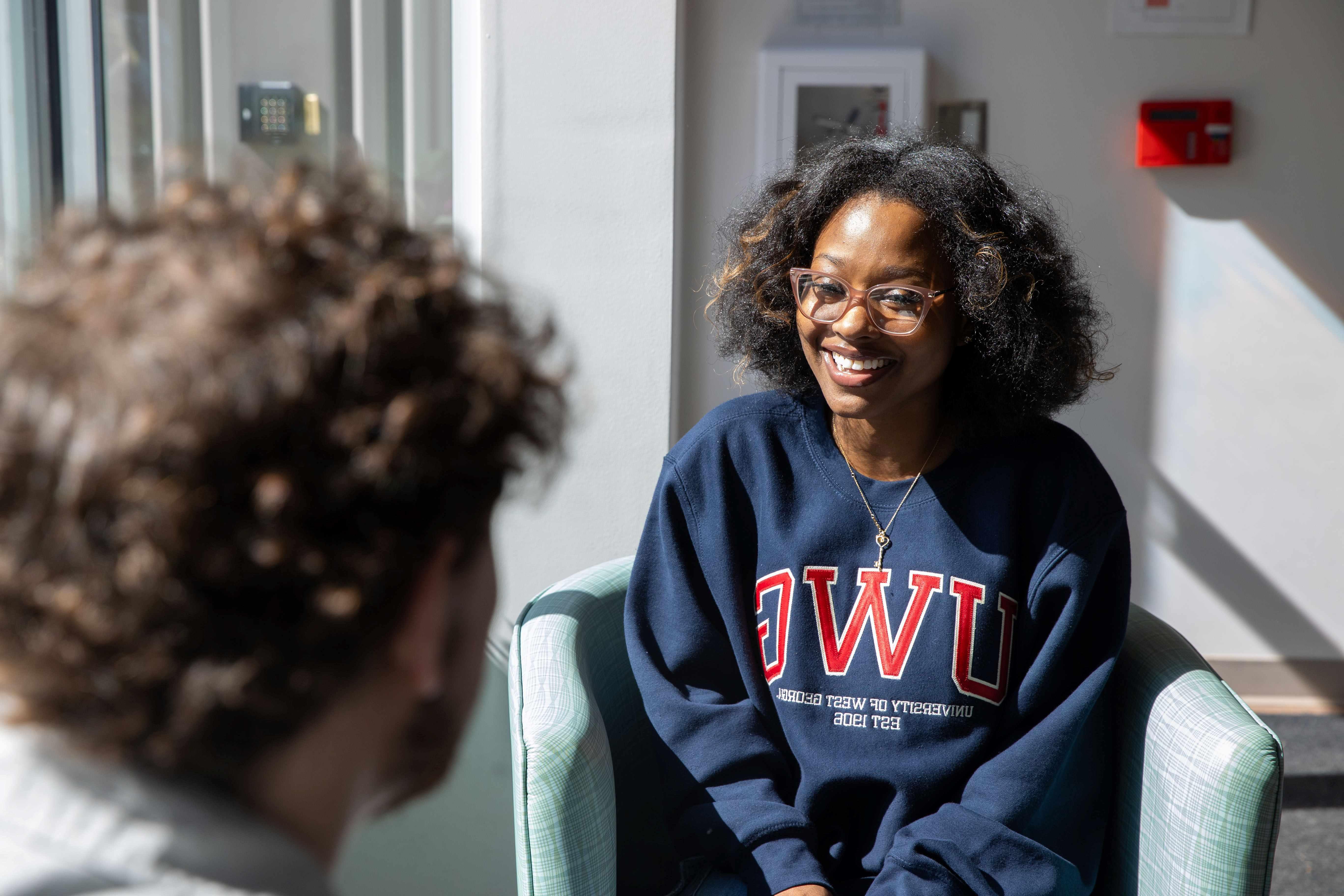 Girl student talking with a guy student while sitting in chairs across from each other. 